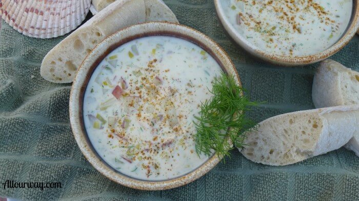 Two brown bowls filled with sheepshead fish chowder with a green sprig of dill on the side of the front bowl, 4 baguette slices surround the bowls that are placed on a green dish towel.