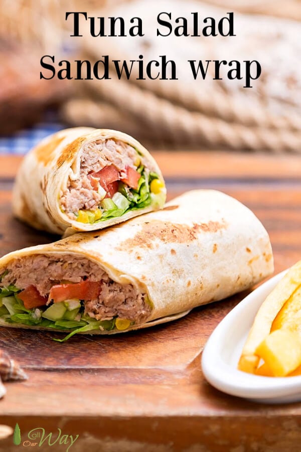 Tuna salad wrap with corn, lettuce, tomatoes, and avocados on a wooden board and a coiled rope in background. 