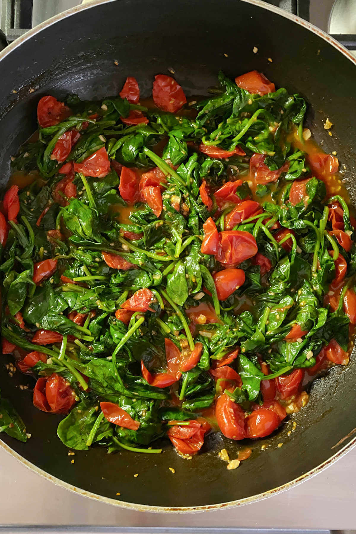 Skillet filled with sauteed baby spinach and grape tomatoes seasoned with garlic and lemon. 