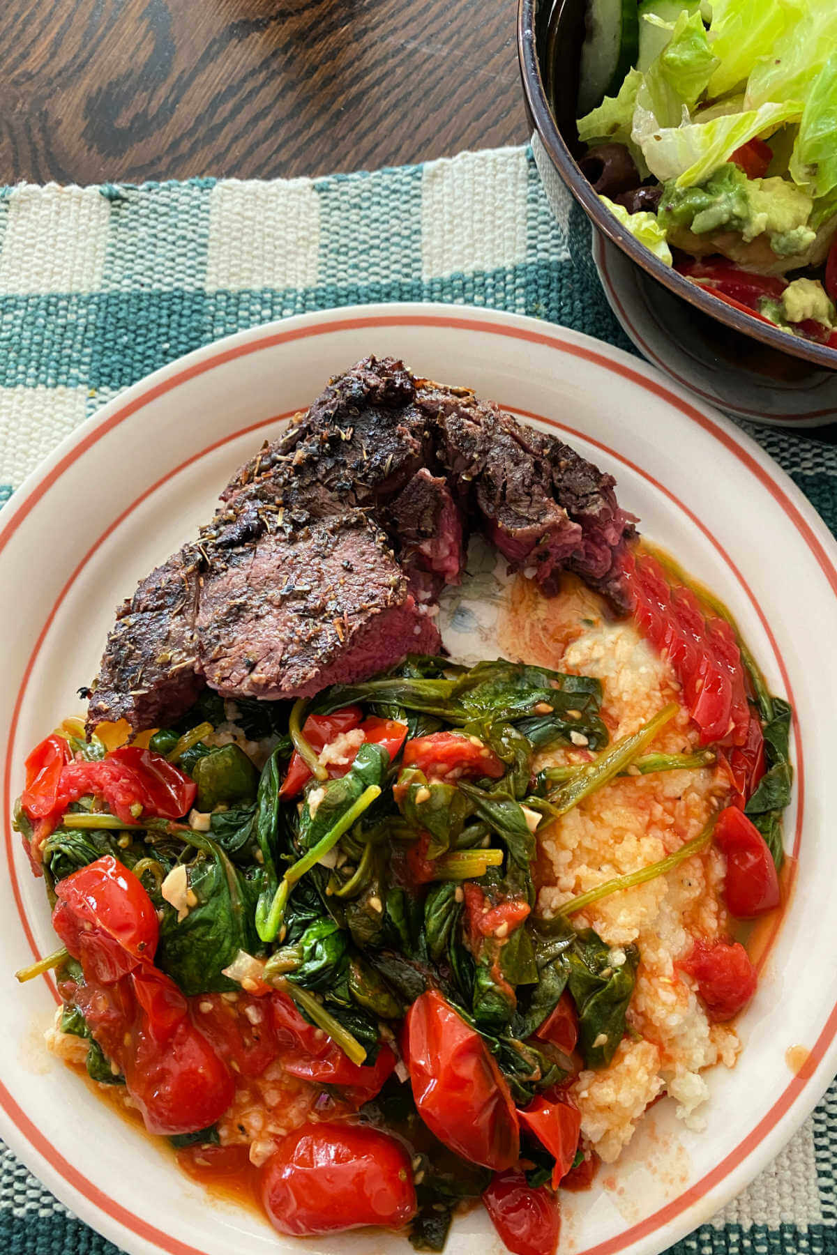Plate with grilled steak and sauteed baby spinach with grape tomatoes over polenta. 