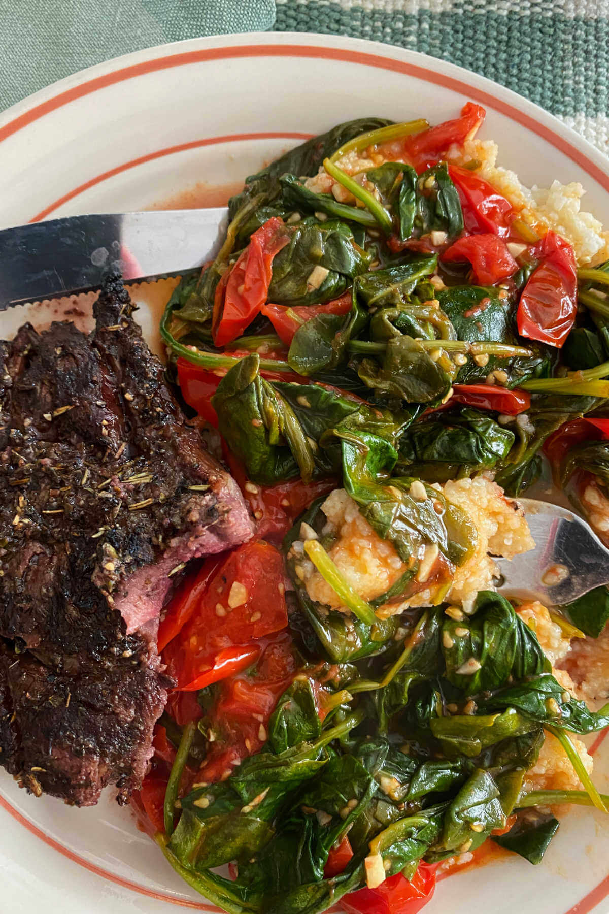 A serving of sauteed baby spinach and grape tomatoes recipe over polenta and grilled steak. 