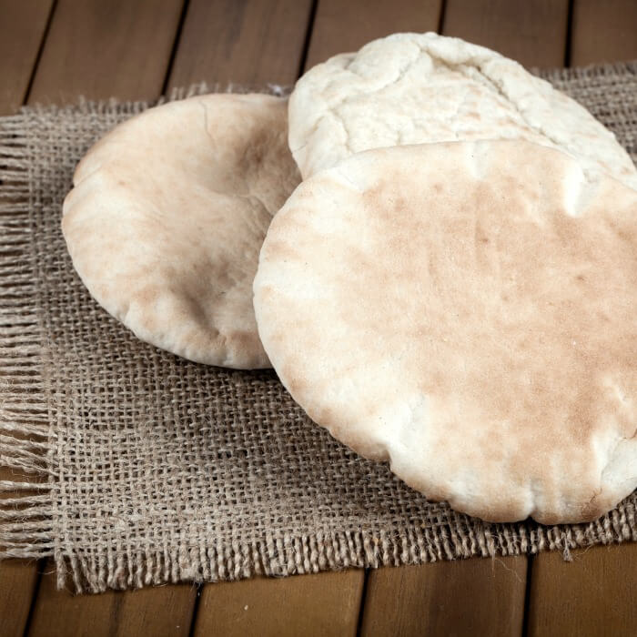 Two pitas lay on a burlap placemat. The pitas are round and lightly browned.