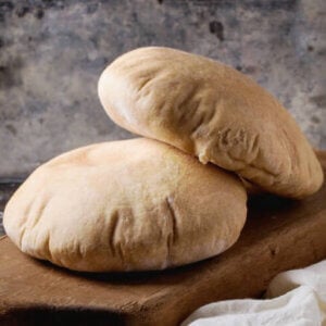 Two pita breads on a dark brown cutting board with white gauze underneath.