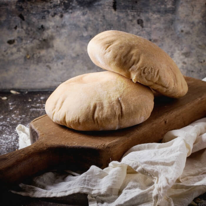 Two pita breads on a dark brown cutting board with white gauze underneath.