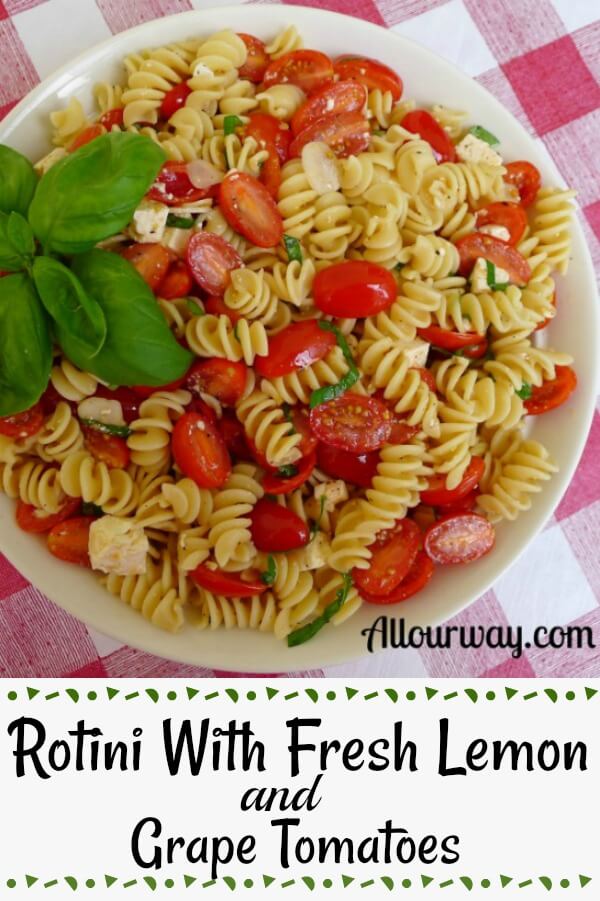 Rotini pasta with halved grape tomatoes, chunks of white ricotta salta in a white bowl on top of a red and white checkered tablecloth.