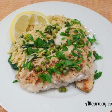 Sea Trout Piccata on a white plate with orzo spinach pasta, lemon wedges, capers, and green parsley.