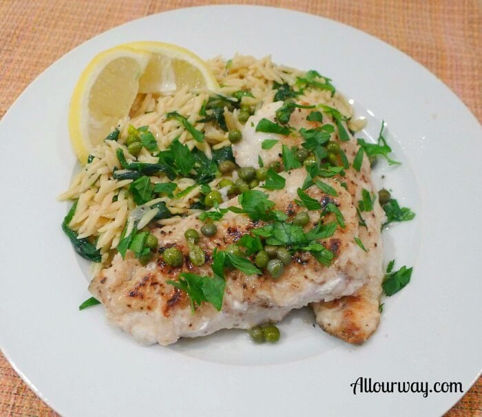 Nicely browned saltwater sea trout piccata with capers, green parsley, and lemon on a white plate. 