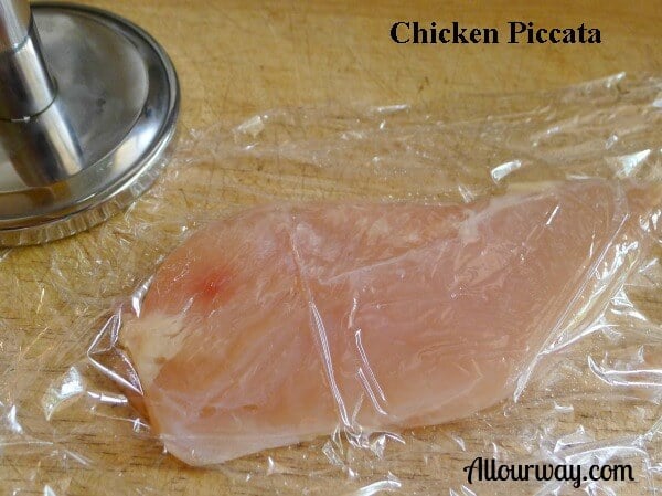 Chicken piccata starts with chicken under saran wrap and flattened with a meat mallet. 