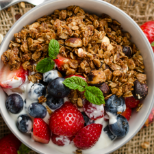 A bowl of homemade granola with blueberries and strawberries in the bowl with yogurt on the side of the granola.