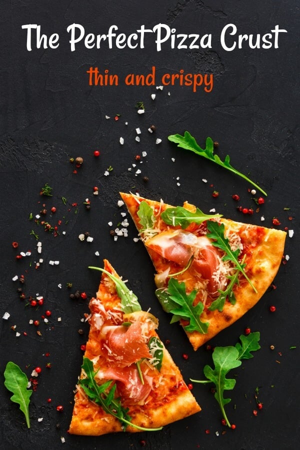 Two slices pizza on black background with hot pepper flakes around pizza and green arugula on top. 