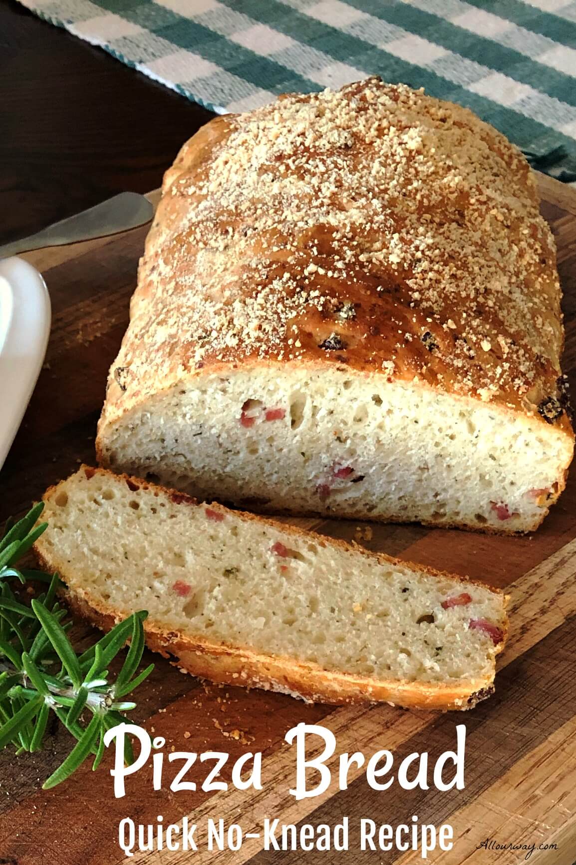 Loaf of golden brown pizza bread sliced on a cutting board with specks of salami and herbs studding the loaf and slice. 