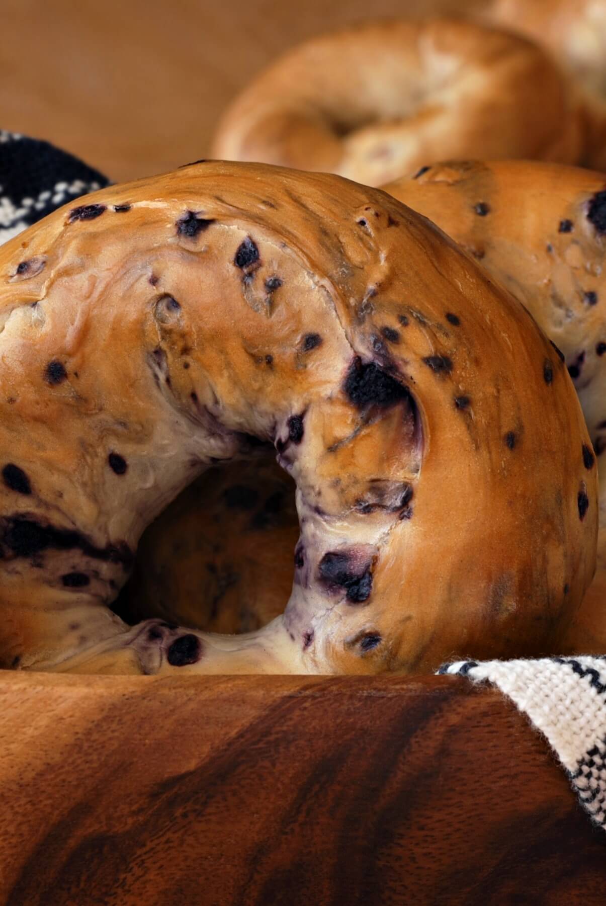 Close up of a fruit nut brown bagel in a white linen lined wooden basket. 