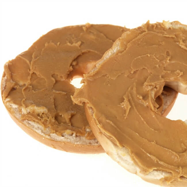 Plain bagel cut in half and slathered with peanut butter on white background. 