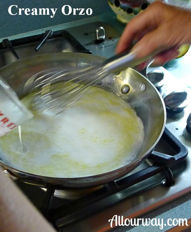 Whisking the creamy orzo sauce in a saucepan on a gas stove. 