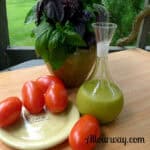 Basil Vinaigrette Salad Dressing in a spouted carafe with tomatoes and a bouquet of basil on the side.