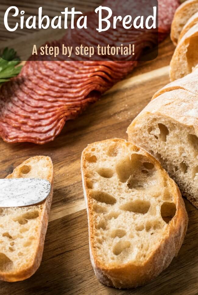 slices of ciabatta bread on wooden breadboard with salami slices and a knife. 