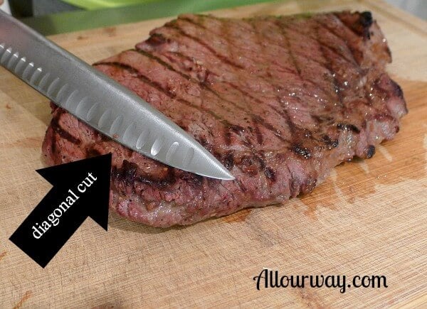 Grilled top round steak on a wooden cutting board with a knife cutting meat on diagonal. 