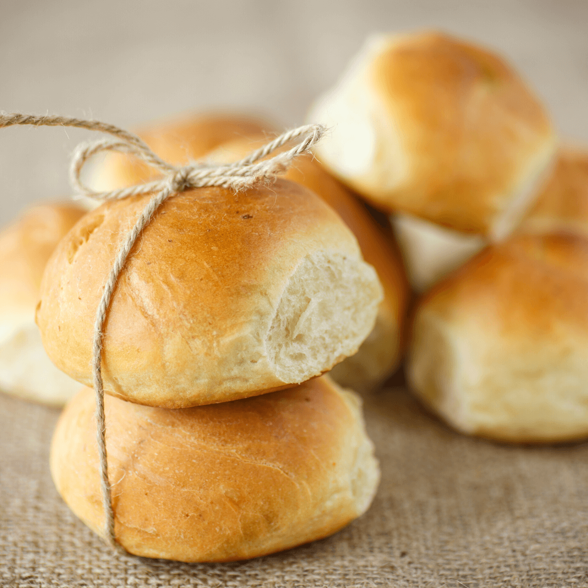 Potato sourdough buns stacked on a table with two tied with twine. 