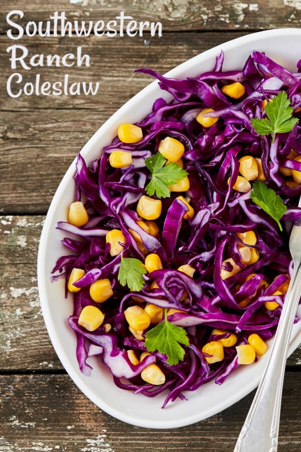 Purple coleslaw and yellow corn with cilantro in a white bowl on rustic wood boards. 