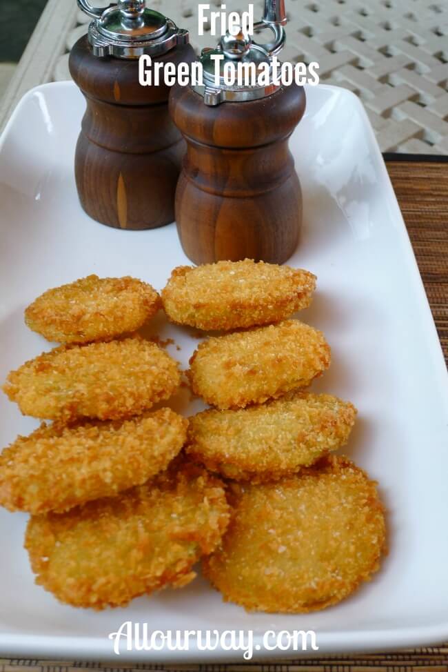 Fried Green Tomatoes Breaded with Panko Crumbs on a white platter with a wooden salt and pepper grinder at the top of the platter.