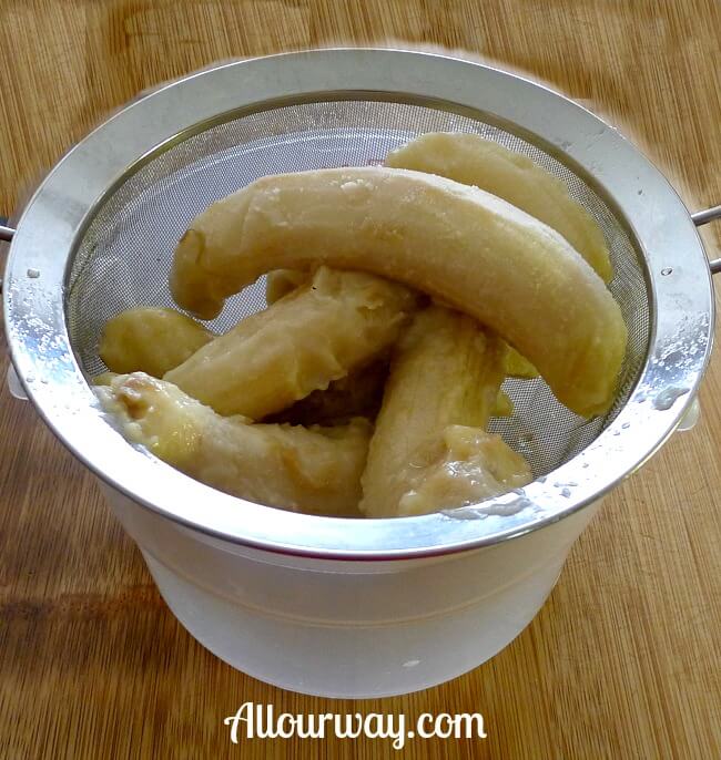 Closeup of frozen bananas in wire sieve over plastic bowl.