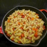 Red bell pepper rotini and bacon in skillet.