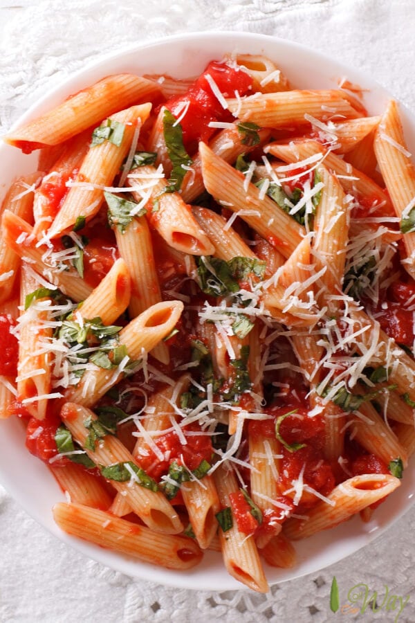 Closeup of penne pasta covered with a red sauce and sprinkled with green herbs in a white bowl. 