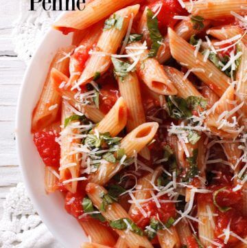 Penne pasta with arrabbiata sauce in a white bowl over a lace edged white table cloth.