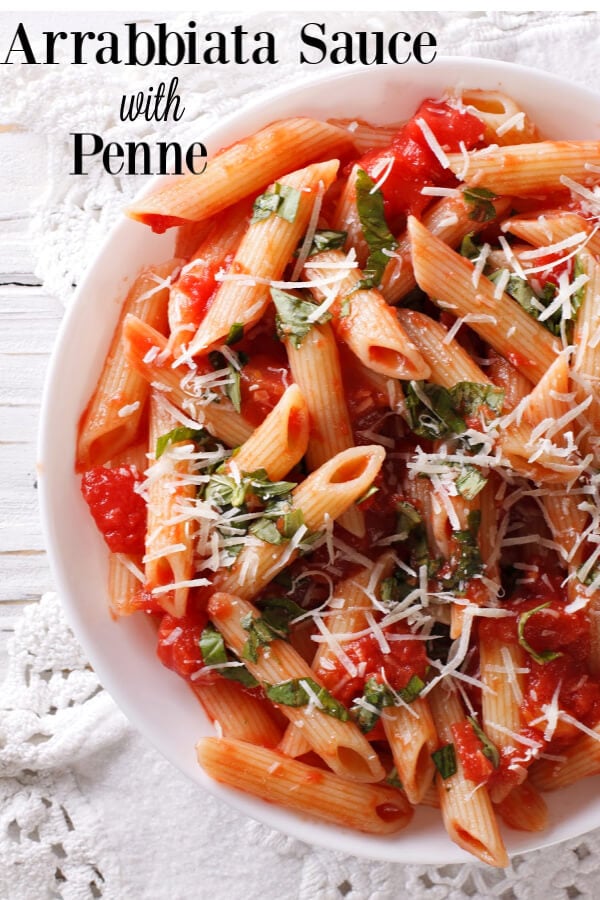 Penne pasta with arrabbiata sauce in a white bowl over a lace edged white table cloth. 