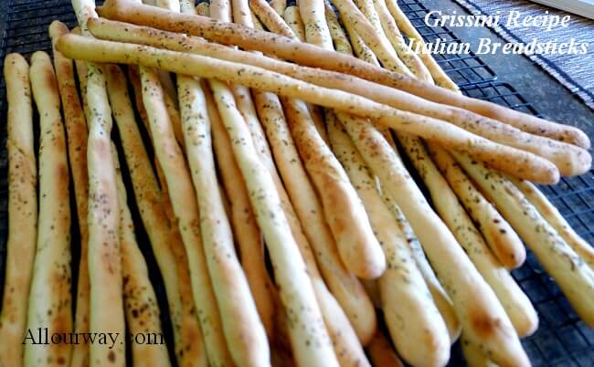 Grissini breadsticks on a black wire rack cooling. The crunchy Italian breadsticks are piled on top of each other. 