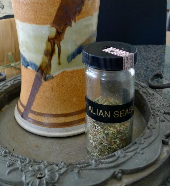 Closeup of a small jar of Grissini breadsticks spicy Italian seasoning for breadsticks. The jar is in front of an orange, white, black and brown pottery vase. 