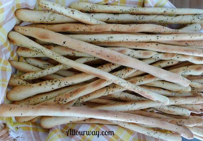 Grissini breadsticks are piled high on a yellow and brown plaid tea towel lined basket. 