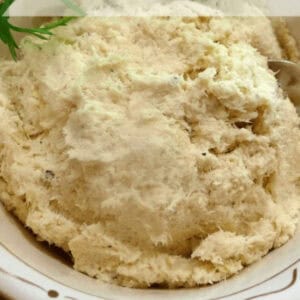 Close-up of creamy baccala in a tan pottery bowl with parsley on the side.