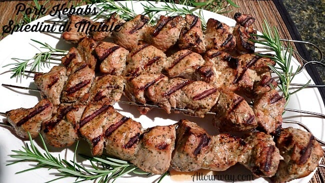 Grilled Pork Kebabs are called Spiedini di Maiale and they are threaded on a skewer and placed on a white platter with rosemary sprigs.