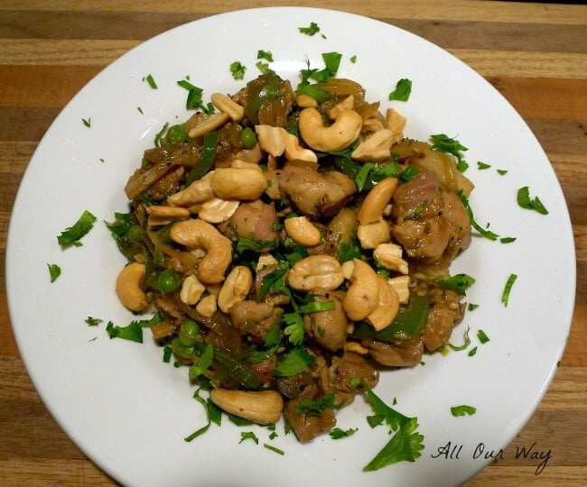 A white bowl full of chipotle chicken stir fry over brown rice with cilantro sprinkled on top. 