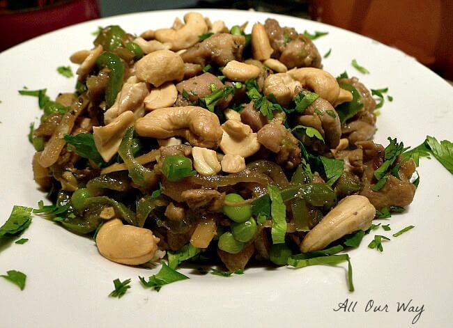 A side view of Chipotle Cashew chicken in a white bowl with peas, cashews, and cilantro on top. 