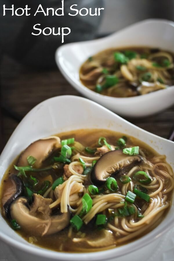 Two triangular white bowls filled with hot and sour soup and sprinkled with green onion rings. 