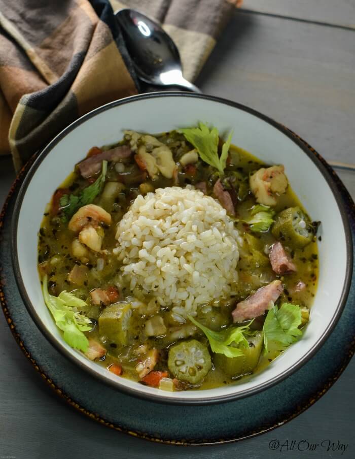 Louisiana shrimp gumbo in brown bowl with a scoop of rice. in the center on top of wood tabletop and brown and black check napkin.