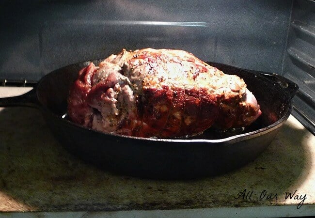 The leg of lamb in black cast iron skillet in oven roasting. 
