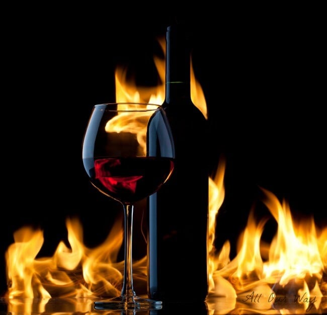 A bottle and glass of red wine in front of a fire. 