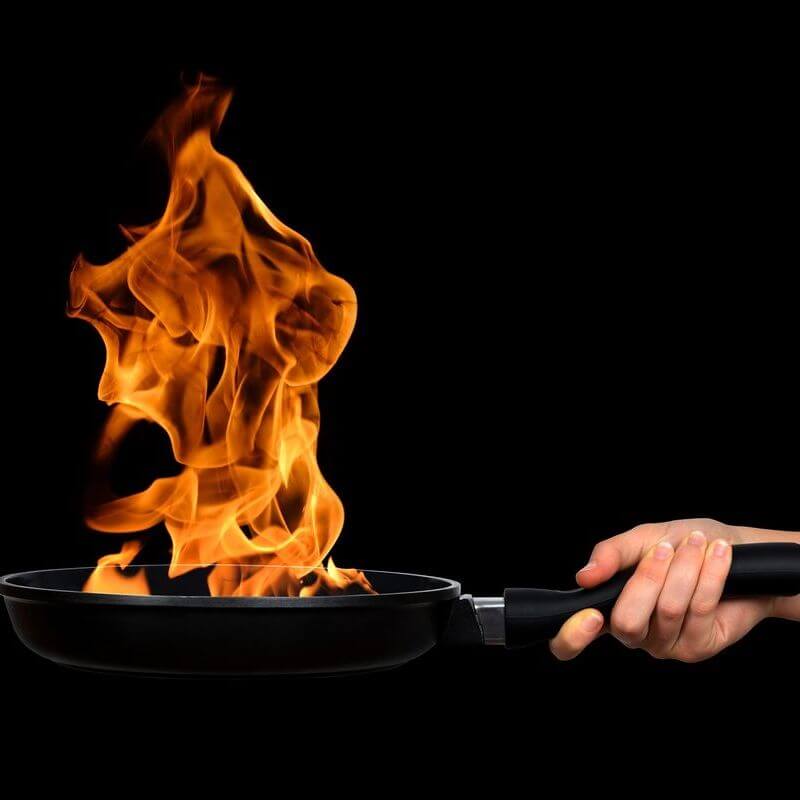 A woman's hand holding a pan with flames coming from it. 