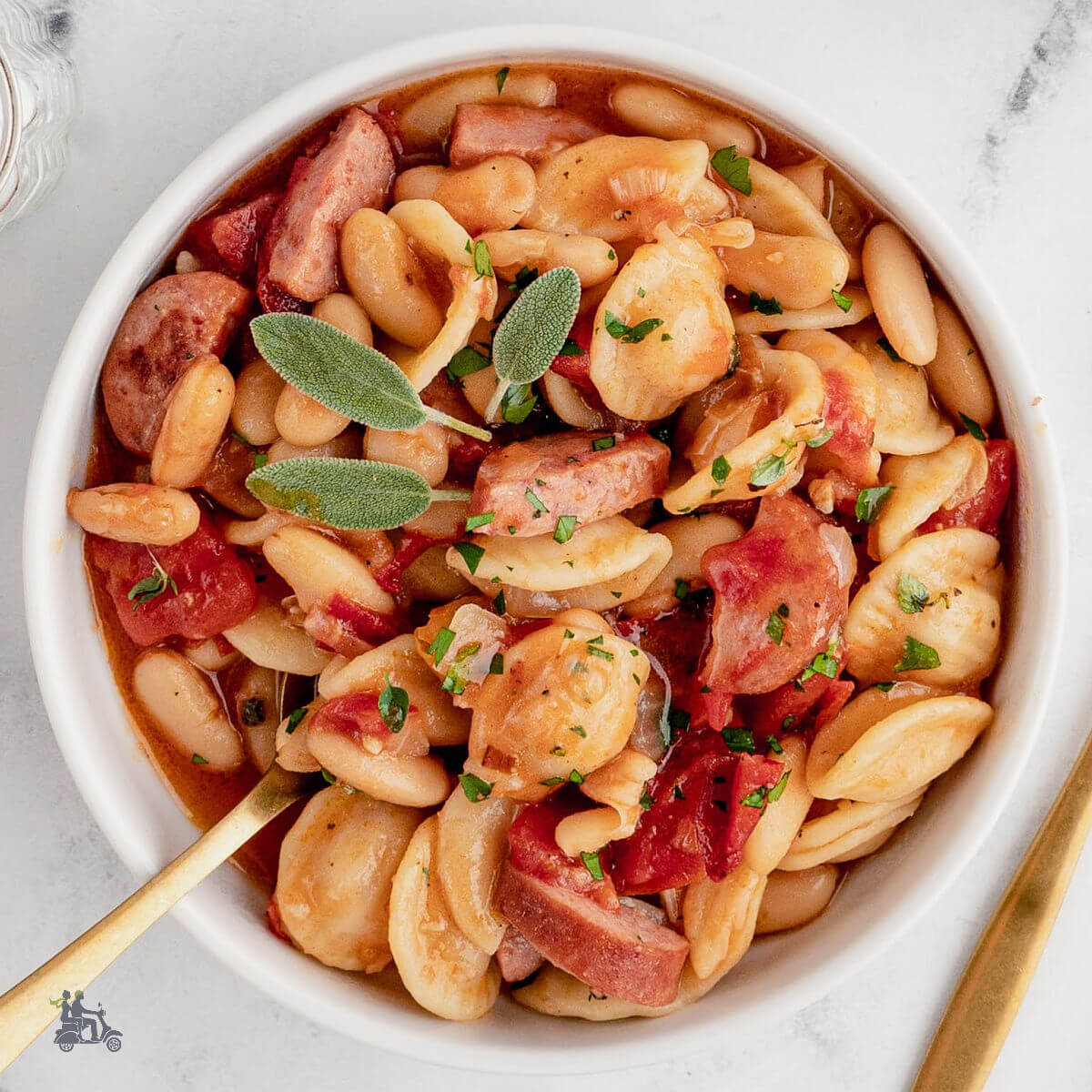 Fagioli Al Forno or Italian Baked Beans in a white bowl with a sage sprig on top.