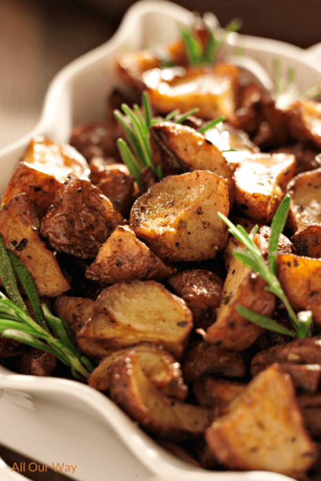 Garlic roasted potatoes in a white casserole dish with sprigs of herbs in the potatoes