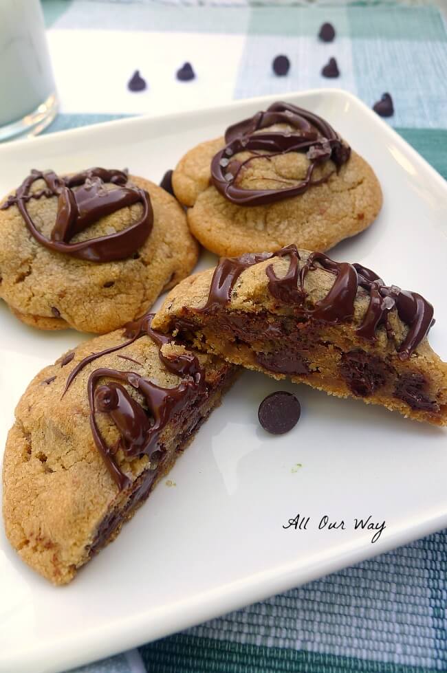 Sweet Salty Nutella Chocolate Chip Cookies with brown butter and sea salt on a white square plate with chips scattered around it all on a green and white plaid placemat. One cookie is split and half showing the nutella filling. @allourway.com