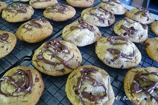 Salty sweet Nutella chocolate chip cookies drizzled with chocolate and sprinkled with coarse sea salt on a black non-stick cooling rack @ allourway.com