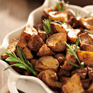 Pommes de terre rôties en quartiers brun doré dans une cocotte à bords festonnés blancs. Brins de romarin avec pommes de terre.