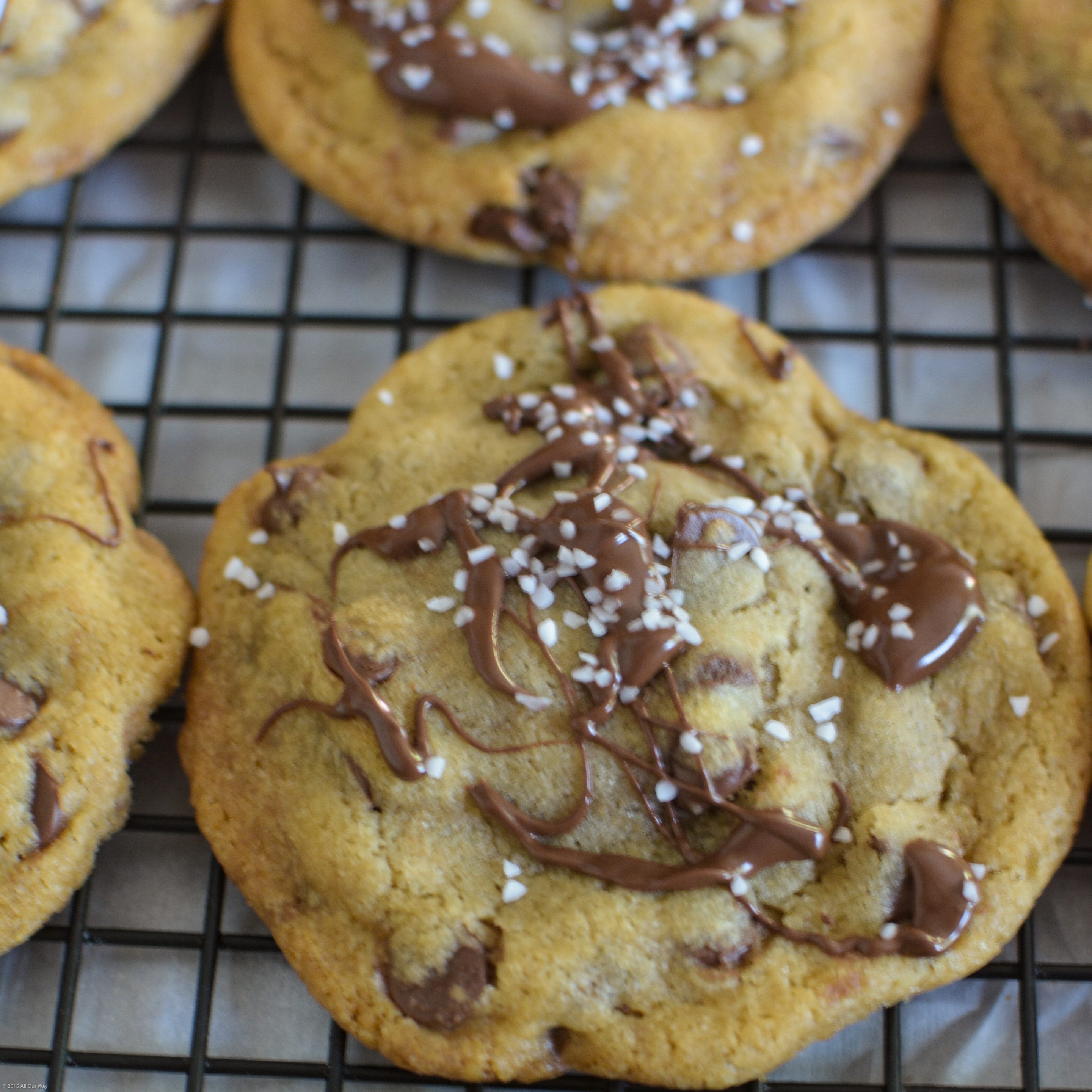 Close up of Salty Sweet Nutella Chocolate Chip Cookies get their nutty flavor from browned butter. On top the drizzle of chocolate is a touch of salt on a black wire cooling rack. 