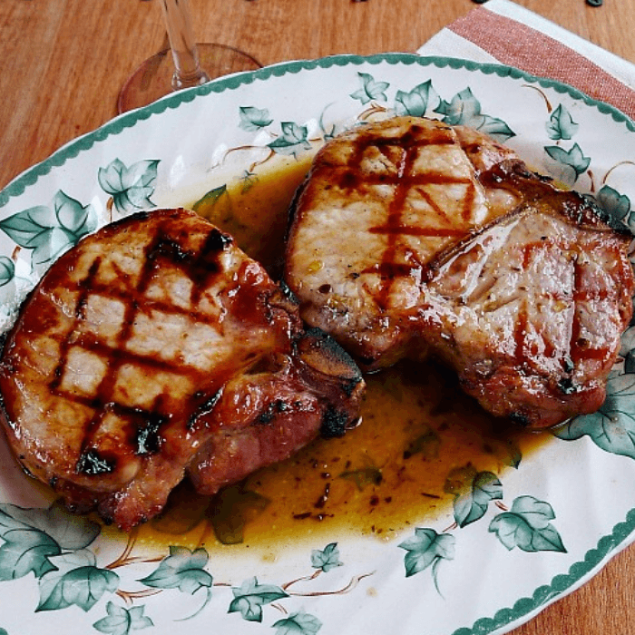 Two grilled pork chops on leaf patterned plate covered with maple glaze