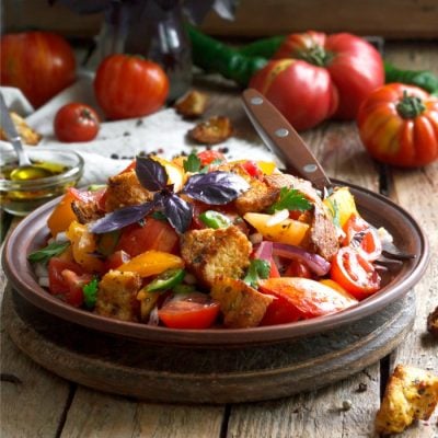 Panzanella an Italian bread salad in dark bowl with fork and tomatoes around it.
