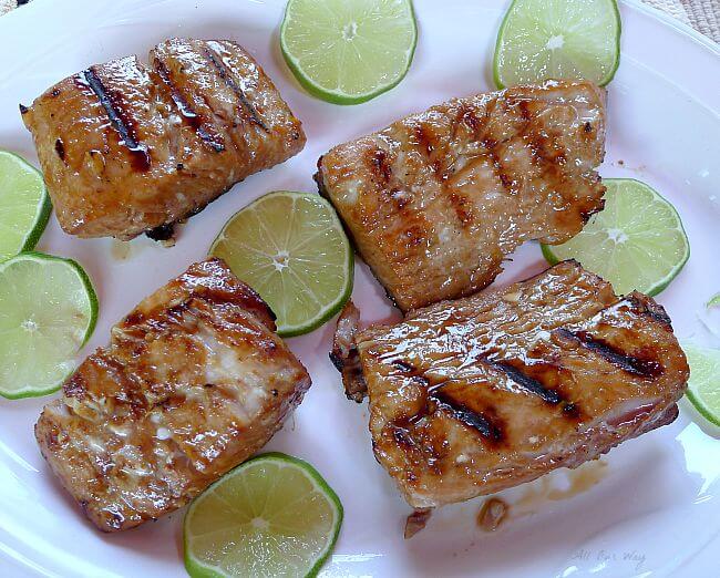 Grilled Lime Marinated Mahi Mahi with grill marks on a white plate with slices of lime surround the 4 fillets. @ allourway.com